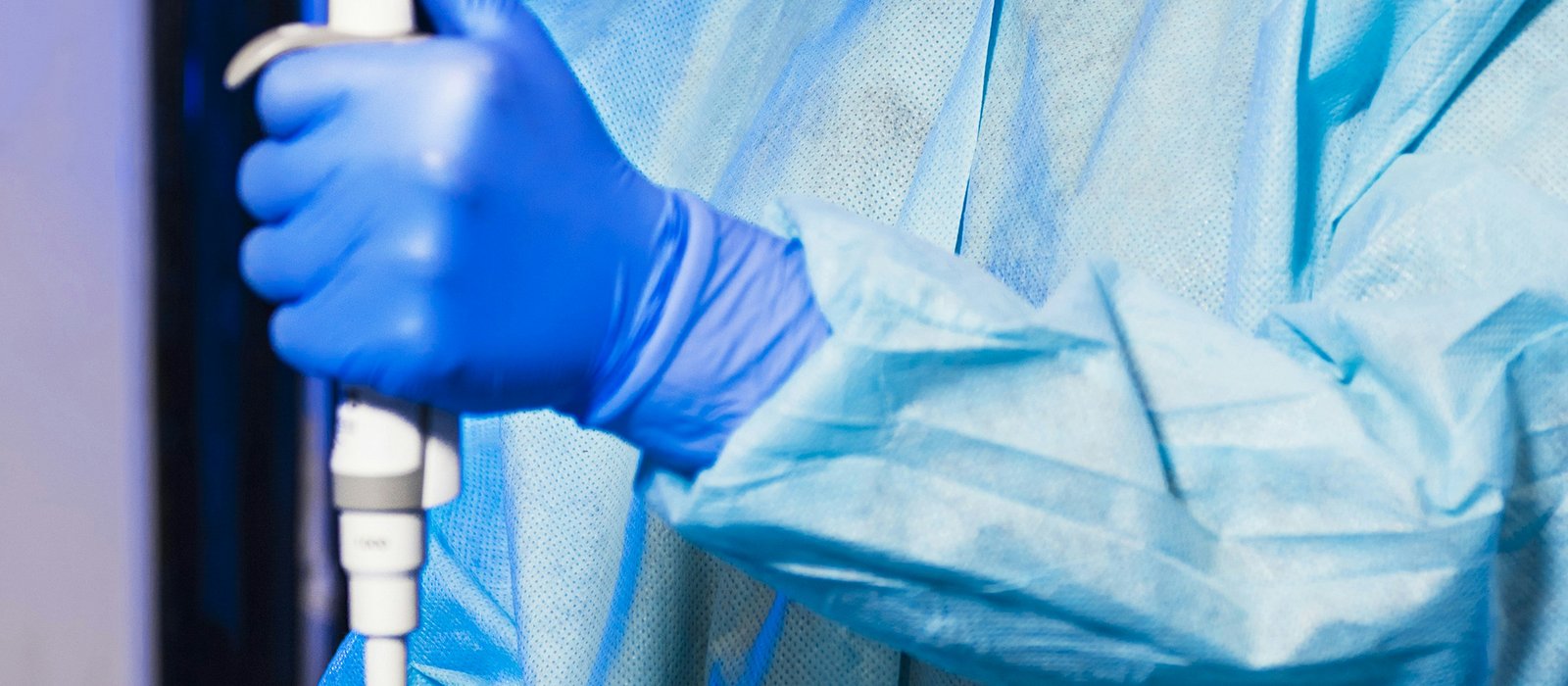 Cercetător cu mănuși albastre folosind o pipetă într-un laborator farmaceutic