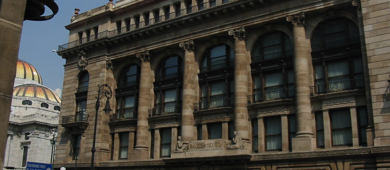 Fațada clădirii Banco de México din centrul Ciudad de México, cu coloane și cupola Palatului Bellas Artes vizibilă în stânga